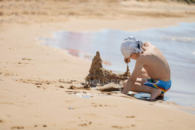 Niño construyendo un castillo de arena en la playa, Corfú, Grecia - foto de stock