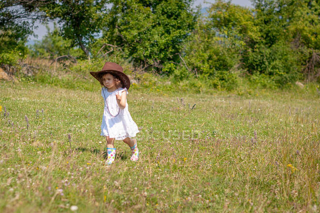 Menina em um vestido de verão e chapéu de cowboy correndo em um prado, Bulgária — Fotografia de Stock