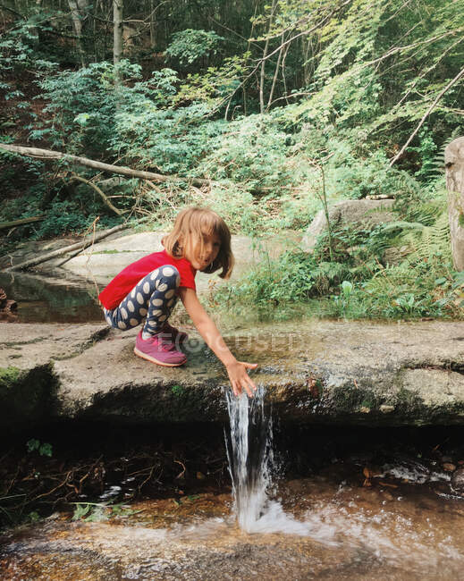 Girl crouching by a creek in the forest, Spain — Stock Photo