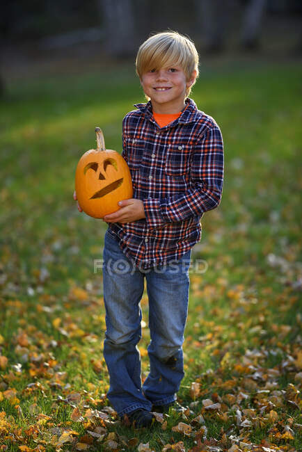 Portrait of a smiling boy standing in the garden holding a jack-o-lantern, Untied States — Stock Photo