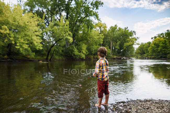 Boy standing by a river fishing, United States — Stock Photo