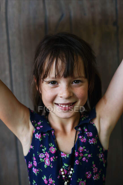 Retrato de una niña sonriente en un vestido de verano con los brazos levantados - foto de stock