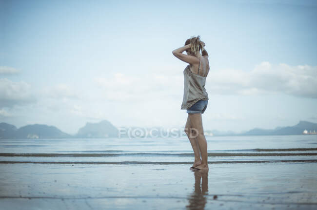 Vista laterale di una donna in piedi sulla spiaggia mettendo i capelli in una coda di cavallo, Koh Yao, Phang Nga, Thailandia — Foto stock