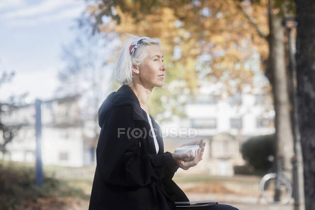 Mujer sentada en el parque con una taza de café - foto de stock