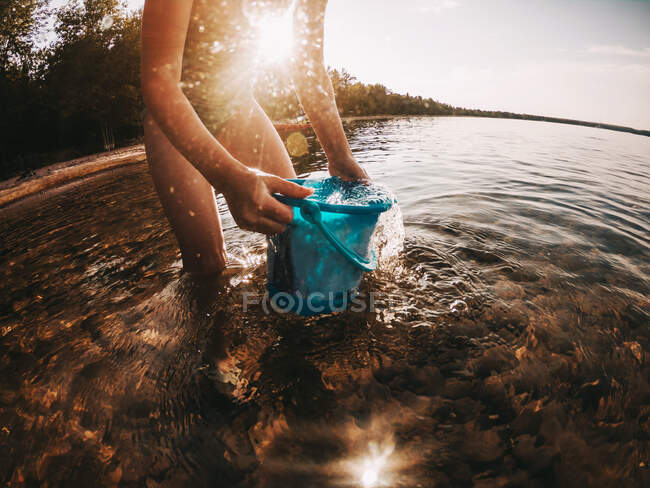 Девушка, стоящая в озере, наполняя ведро водой, озеро Верхнее, США — стоковое фото