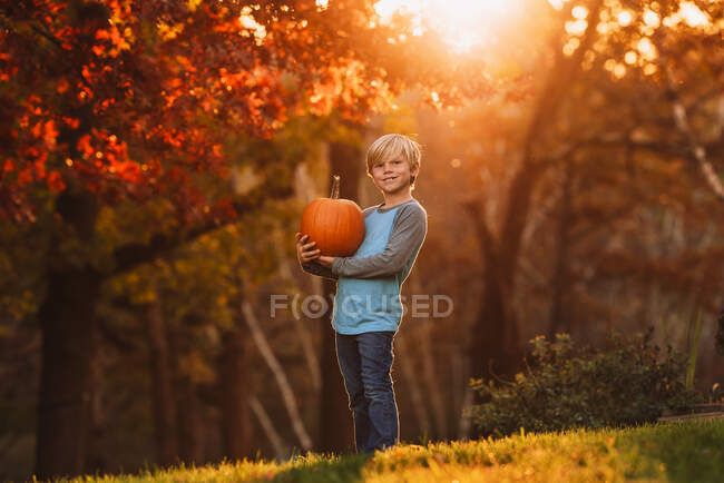 Хлопець стоїть у саду з гарбузом (США). — стокове фото
