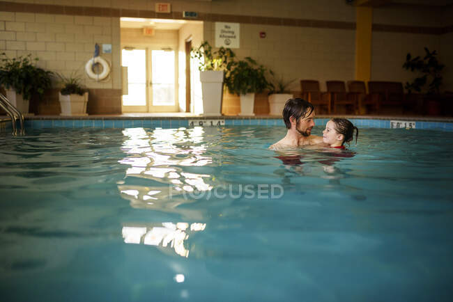 Padre sosteniendo a su hija en una piscina - foto de stock