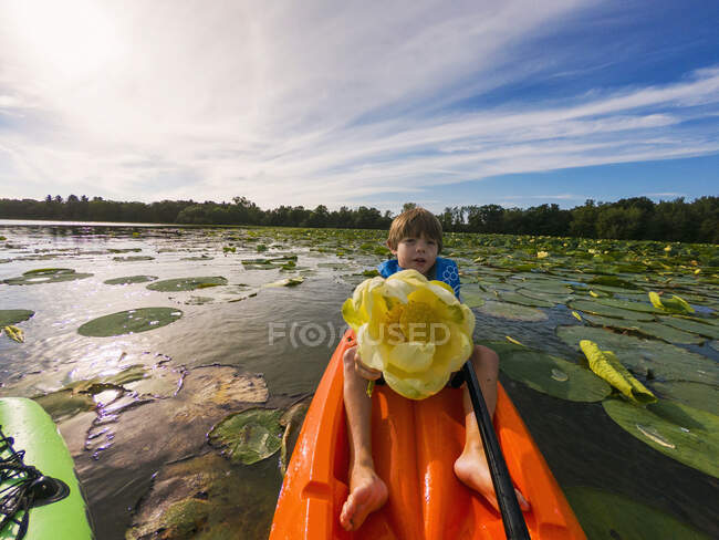 Menino no caiaque segurando flor de lírio na cena do lago — Fotografia de Stock