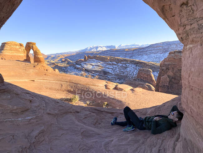Hombre sonriente relajante, Arco Delicado, Parque Nacional Arches, Utah, Estados Unidos - foto de stock
