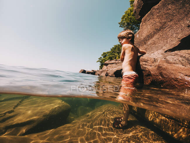 Boy standing in a lake holding onto rocks, Lake Superior, United States — Stock Photo