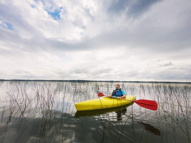 Смиллинг пожилой женщины на байдарке на озере, США — стоковое фото