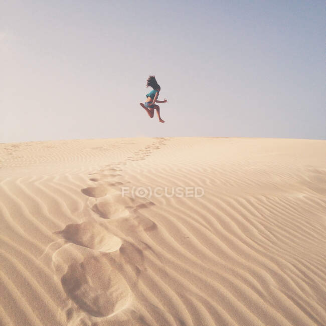 Mujer saltando en el aire sobre dunas de arena, España - foto de stock