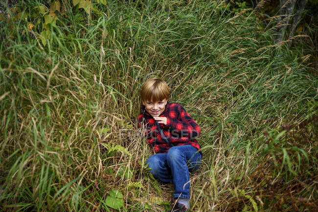 Lächelnder Junge mit Stichen im Gesicht, der im langen Gras sitzt, Lake Superior Provincial Park, USA — Stockfoto