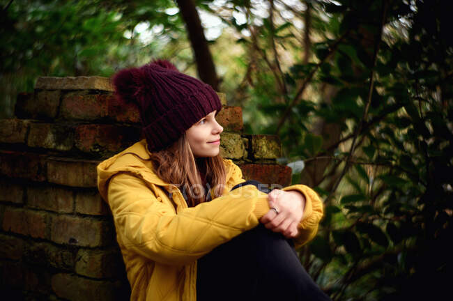 Chica sonriente sentada en una pared en otoño, Irlanda - foto de stock