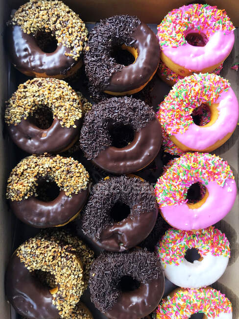 Overhead view of a box of assorted doughnuts with icing and sprinkles — Stock Photo