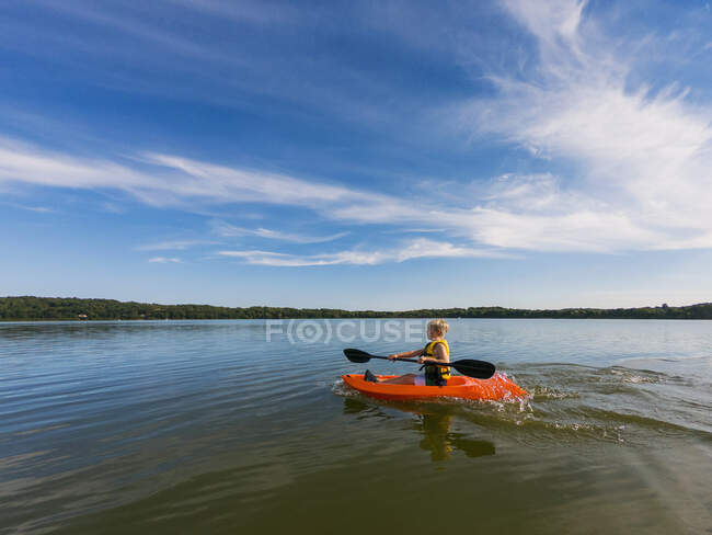 Хлопчик кашляє на озері під хмарним блакитним небом. — стокове фото
