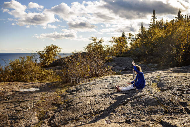 Niña sentada sobre rocas sosteniendo un palo, Lake Superior Provincial Park, Estados Unidos - foto de stock