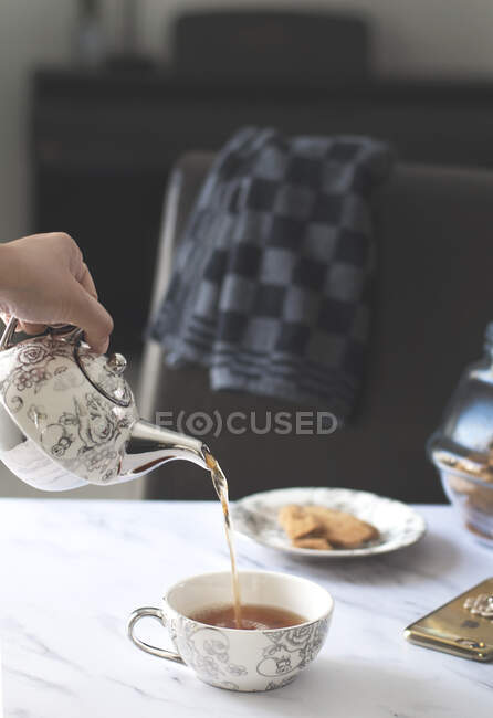 Main humaine versant une tasse de thé — Photo de stock