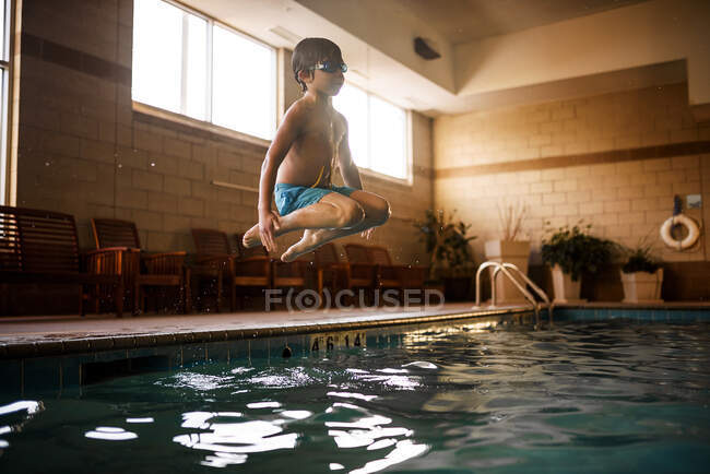 Garçon portant des lunettes sous-marines sautant dans la piscine — Photo de stock