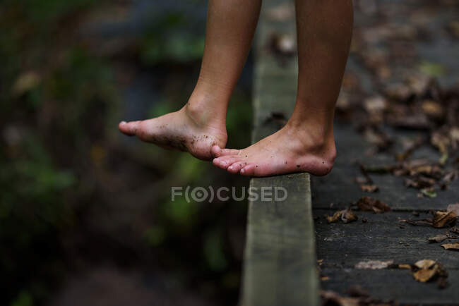 Close-up of a boy's dirty feet standing on a footbridge in the forest, United States — Stock Photo