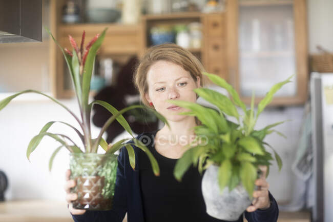 Donna in piedi in cucina con due piante in vaso — Foto stock
