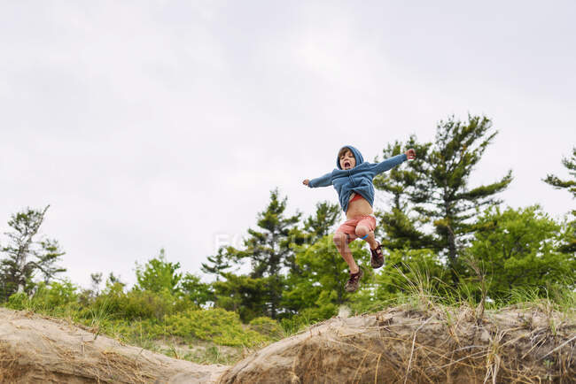 Мальчик прыгает на вершину холма в зеленой сцене под облачным небом — стоковое фото