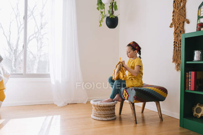 Girl sitting on a stool opening her backpack — Stock Photo