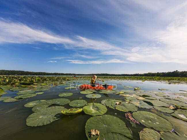 Мальчик плавает на байдарках по озеру, наполненному водяными лилиями — стоковое фото