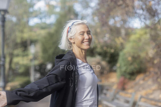 Усміхнена старша жінка в парку з простягнутими руками — стокове фото