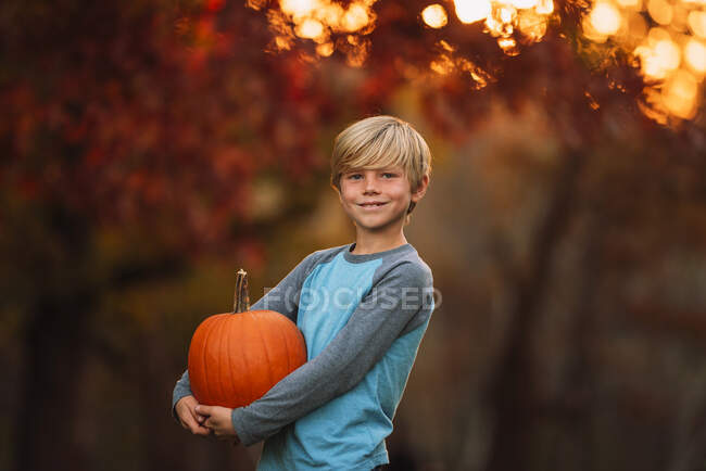 Retrato de um menino de pé em um jardim carregando uma abóbora, Estados Unidos — Fotografia de Stock