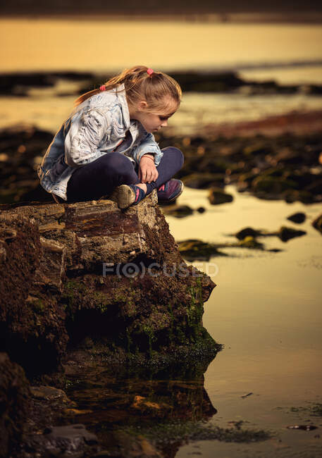 Fille assise sur un rocher côtier regardant dans l'océan, Irlande — Photo de stock