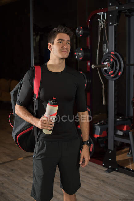 Portrait of a man standing in a gym holding a water bottle — Stock Photo