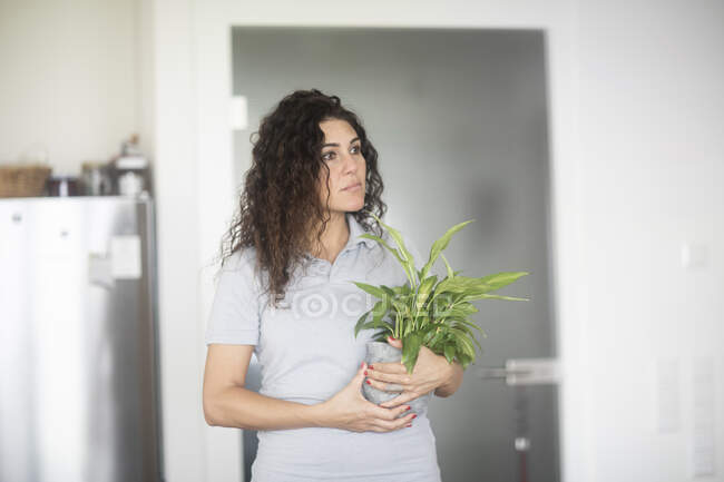 Жінка стоїть на кухні, що тримає горщик рослини — стокове фото