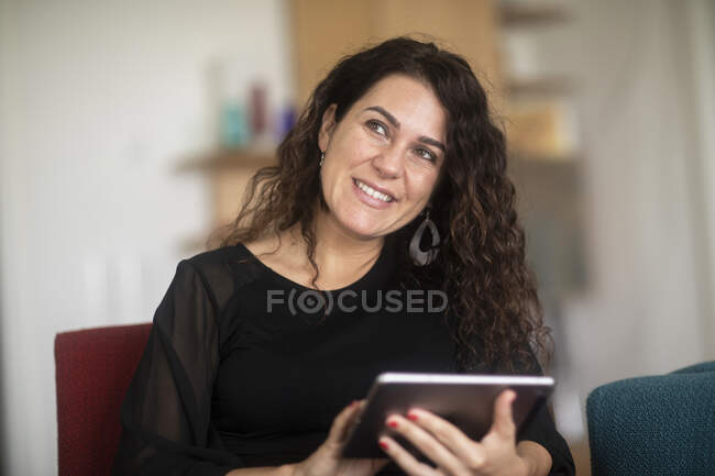 Усміхнена жінка сидить на дивані за допомогою цифрового планшета — стокове фото