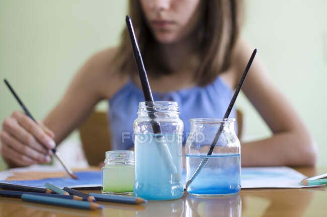 Menina sentada a uma mesa de pintura com aquarelas — Fotografia de Stock