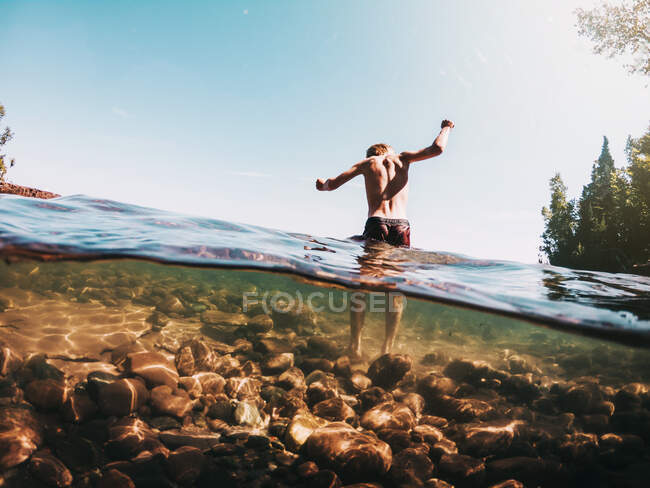 Visão traseira de um menino andando sobre rochas em um lago, Estados Unidos — Fotografia de Stock