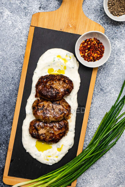 Overhead view of Georgian Abkhazura spicy fried meatballs on a bed of sour cream with red chilli flakes and black pepper — Stock Photo