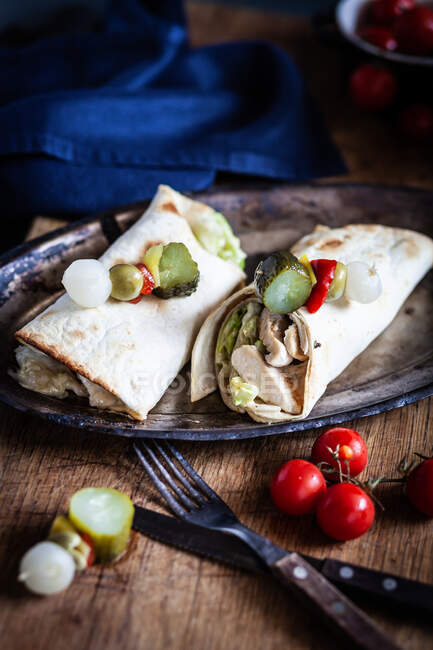 Two chicken wraps on a plate with gherkin, olive and pickled onion garnish — Stock Photo