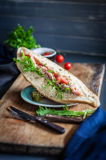 Ham, tomato and rocket sandwich with a gherkin on a chopping board in the kitchen — Stock Photo