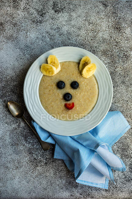 Overhead view of a bowl of oatmeal decorated with fresh fruit to look like a bear's face — Stock Photo