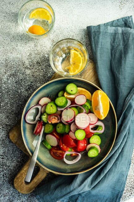 Dois copos de água de limão e uma tigela de pepino, tomate, cebola vermelha e salada de rabanete — Fotografia de Stock