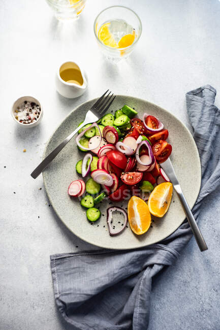 Insalata di pomodoro, cetriolo, cipolla rossa e ravanello con un bicchiere di acqua al limone — Foto stock