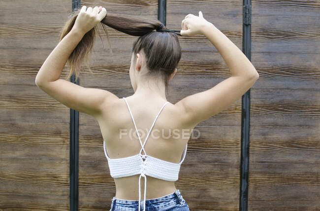 Rear view of a teenage girl standing outdoors putting her hair in a ponytail — Stock Photo