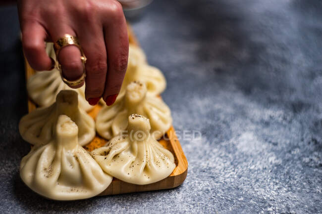 Woman sprinkling black pepper on traditional Georgian khinkali dumplings — Stock Photo