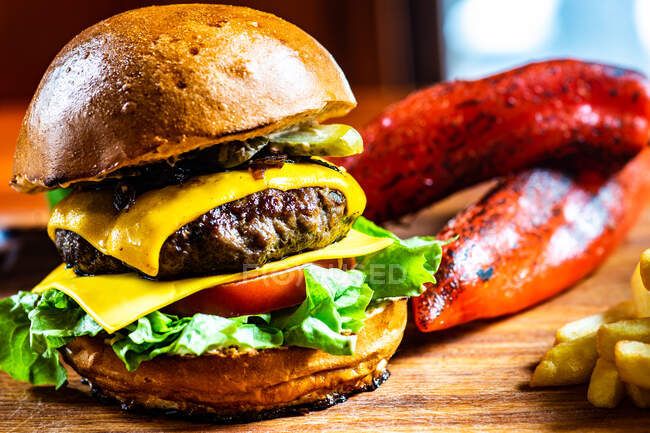 Close-up de um cheeseburger com tomate, pepino e alface servido com batatas fritas e pimentas vermelhas assadas — Fotografia de Stock