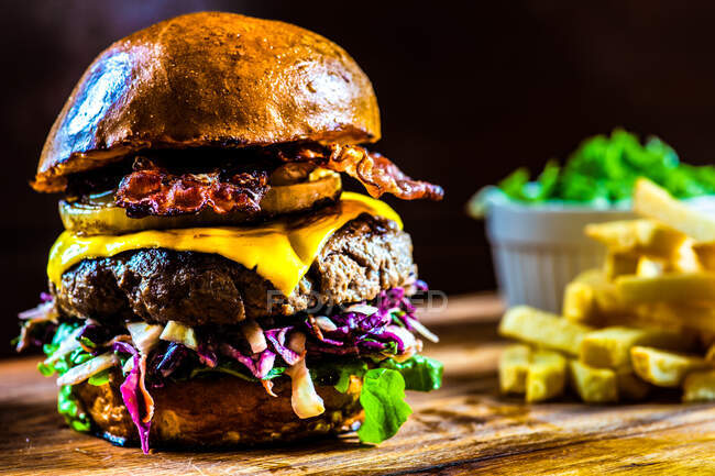 Close-up of a Texas hamburger with cheese, bacon and cabbage salad served with chips on a wooden chopping board — Stock Photo