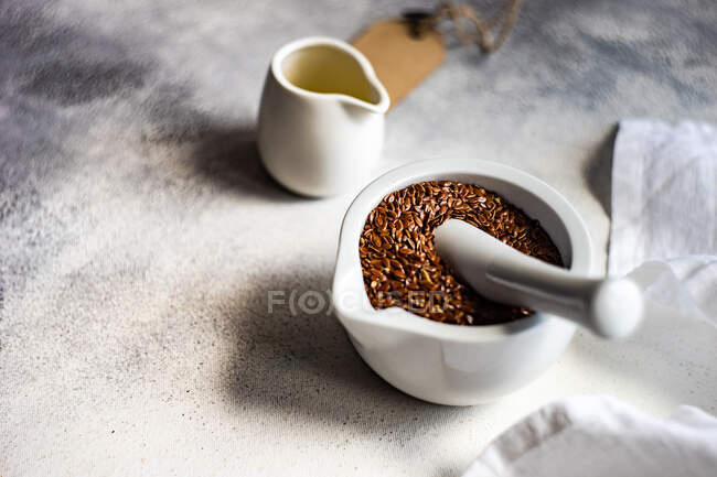 Sementes frescas de linho numa argamassa e num pilão com um jarro de azeite — Fotografia de Stock