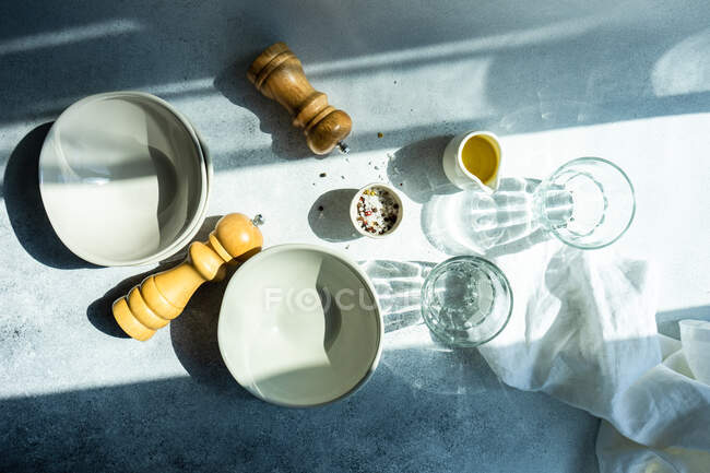 Вид сверху на посуду, стаканы и приправы на столе при солнечном свете — стоковое фото