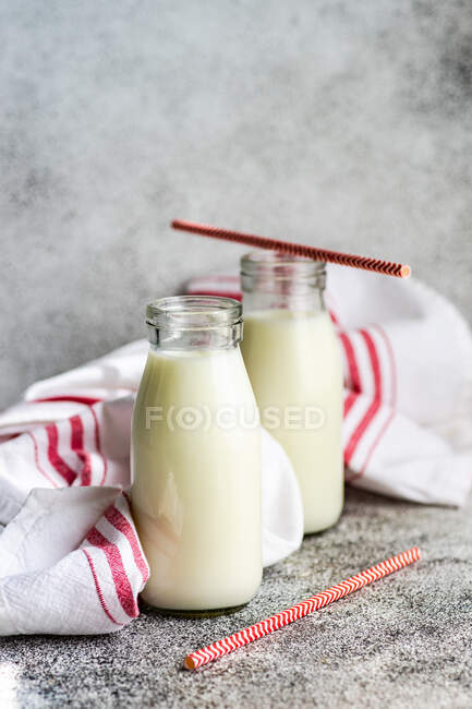 Two bottles of milk and drinking straws on table next to a tea towel — Stock Photo