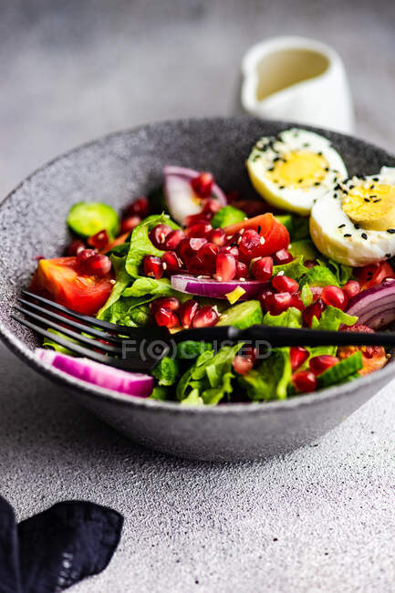 Ensalada con lechuga, tomate, cebolla roja, semillas de granada y un huevo duro con semillas de sésamo - foto de stock